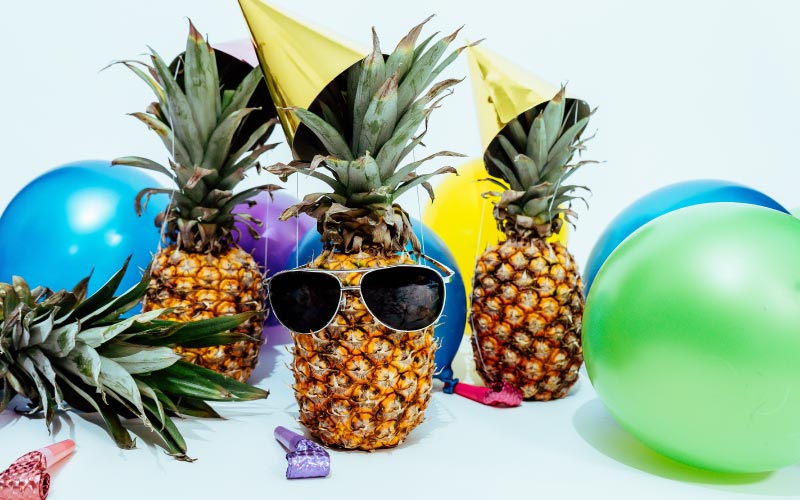 Cluster of pineapples with yellow party hats, noise makers, balloons, and a pair of black sunglasses