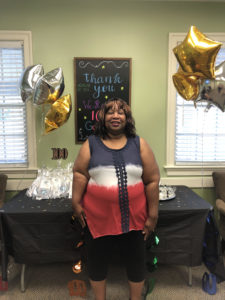 A female patient wearing red, white and blue standing in front of a table at the 100 Google reviews party