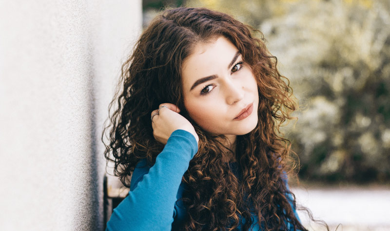 Curly-haired woman wearing a blue shirt rests on her elbow as she thinks about sedation to calm her dental anxiety